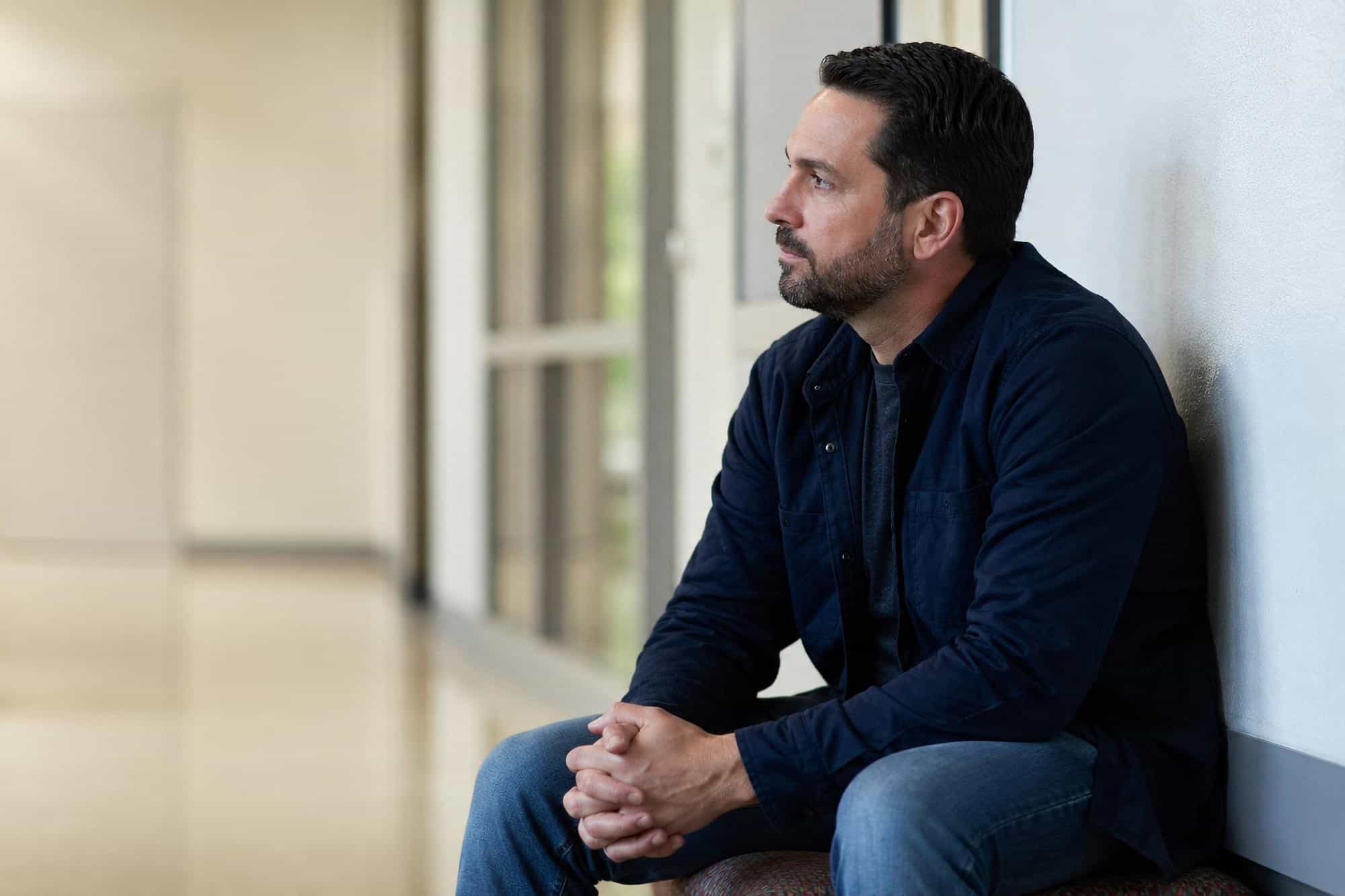 Man sitting and reflecting in a recovery center corridor during behavioral health treatment in Bowling Green, KY at Redstone Behavioral Health.